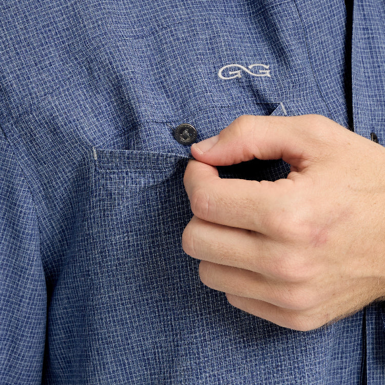 Close-up of a person buttoning a blue checkered shirt with a brand logo.