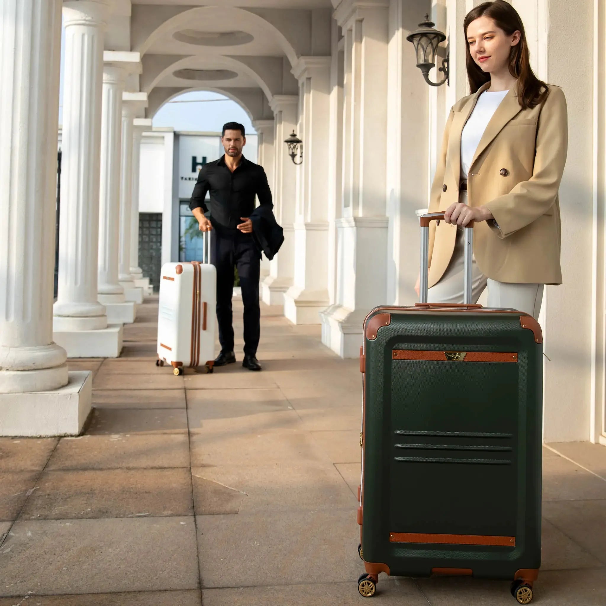 Two people with suitcases walking through a colonnaded building entrance.