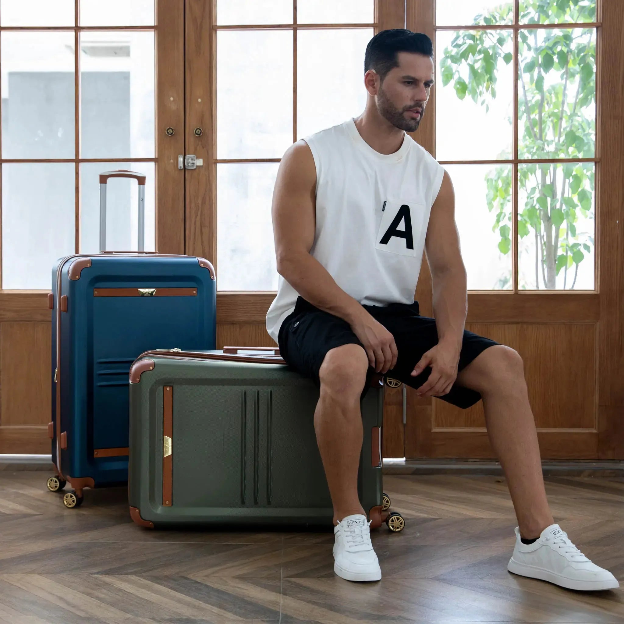 Man sitting on a green suitcase with two other suitcases in the background.