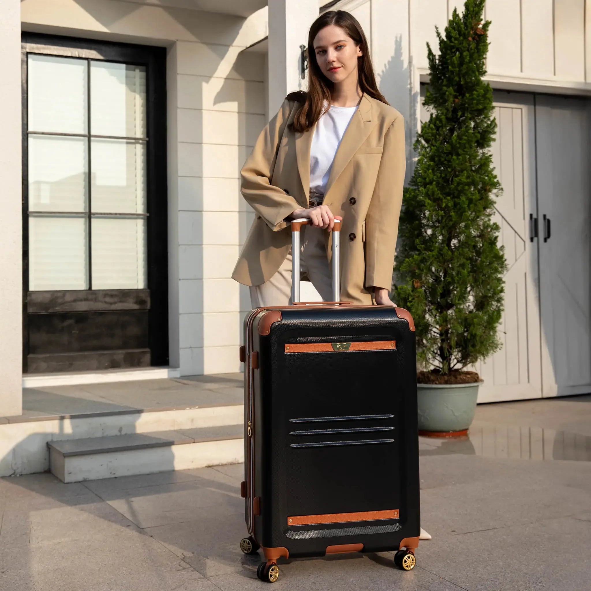 Woman holding a black suitcase with brown accents in front of a building.