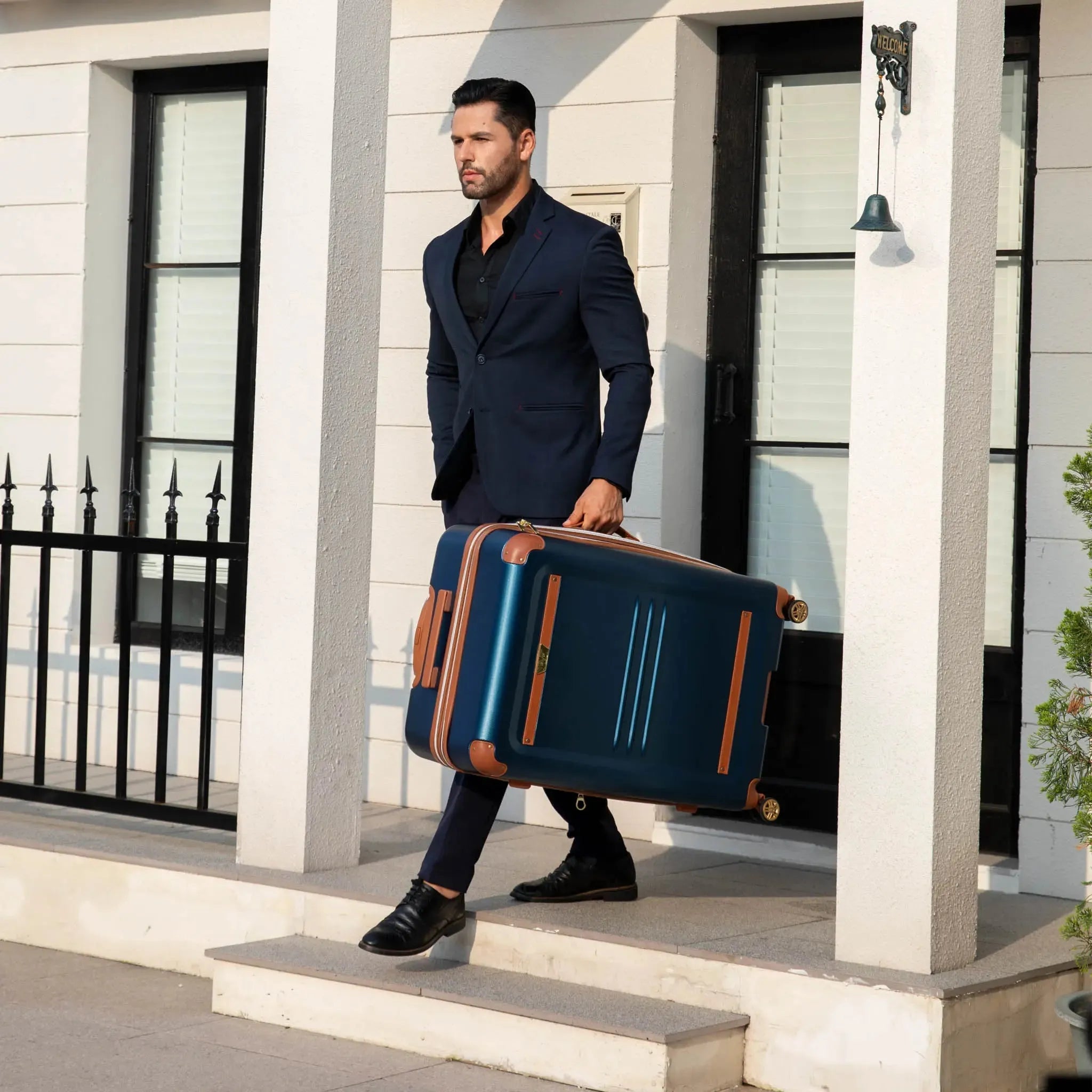 Man in a suit carrying a large blue suitcase outside a building