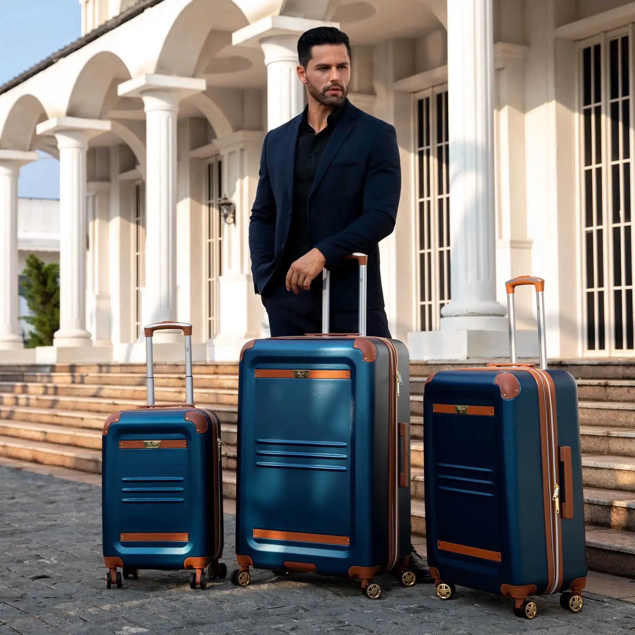 Man standing with three blue suitcases in front of a classical building
