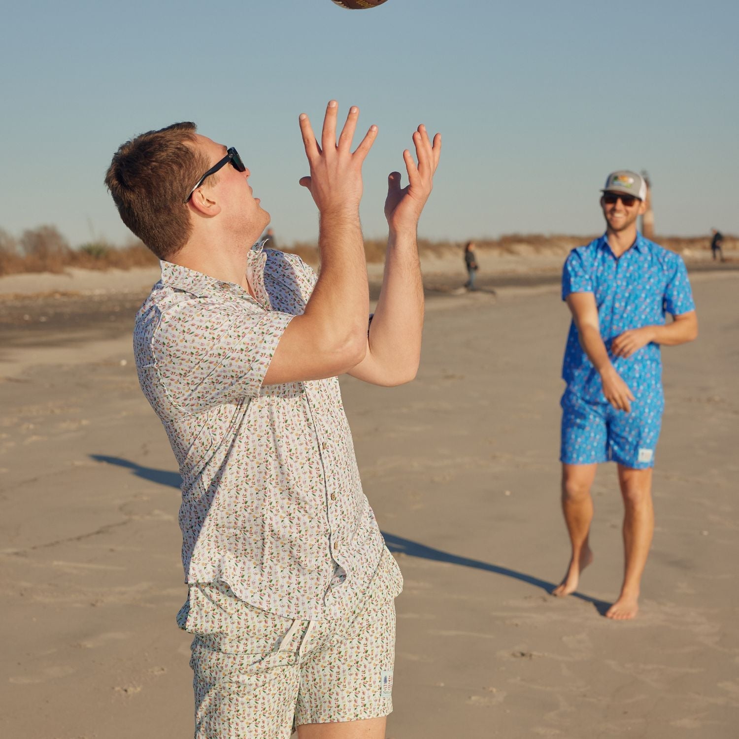 Two men playing frisbee on a sandy beach with clear skies.