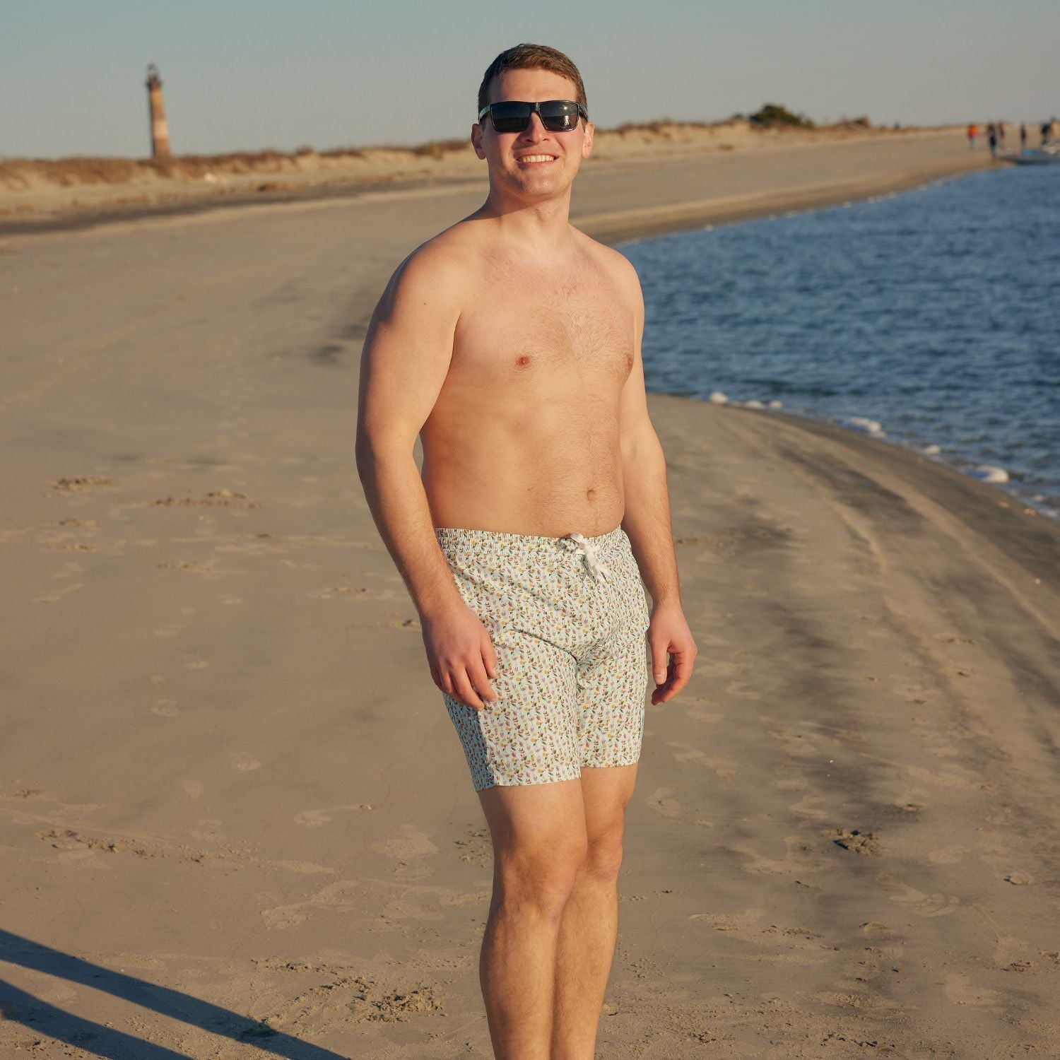Man standing on a sandy beach with ocean and lighthouse in the background