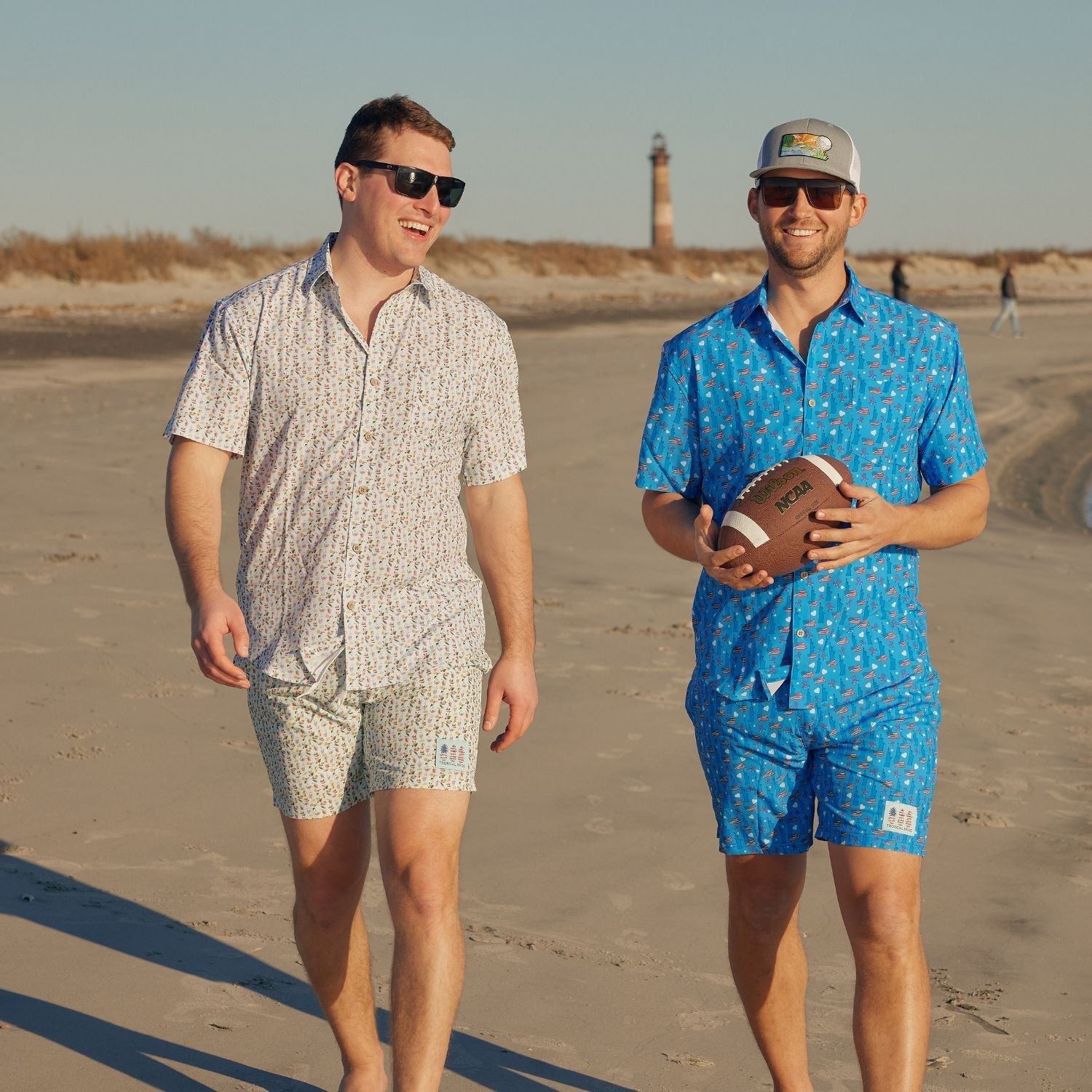 Two men walking on a beach with a lighthouse in the background