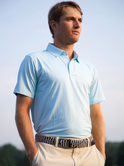 Man wearing a light blue polo shirt and beige pants against a clear sky.
