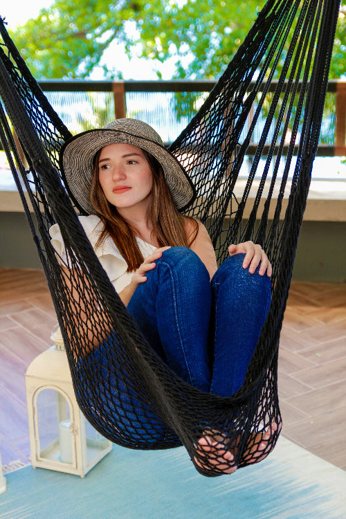 Woman sitting in a black hammock on a balcony with greenery in the background
