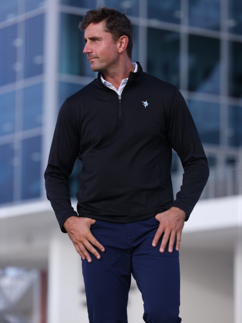 Man wearing a black quarter-zip pullover with a logo in front of a modern building.