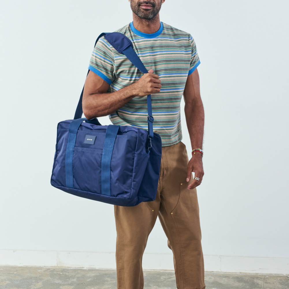 Man holding a blue duffel bag against a light background