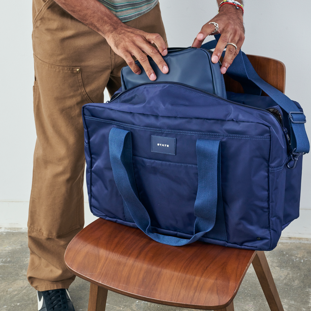 Person opening a blue bag on a wooden chair with a neutral background