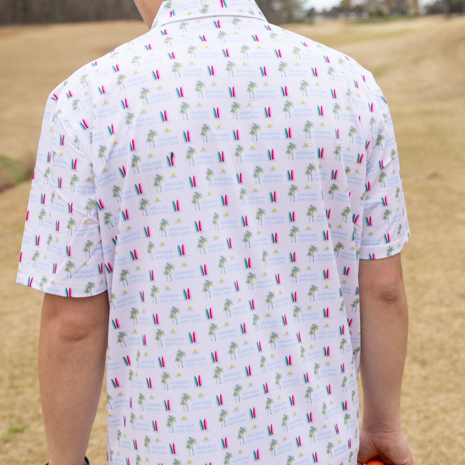 Person wearing a white polo shirt with colorful pattern standing on a golf course.