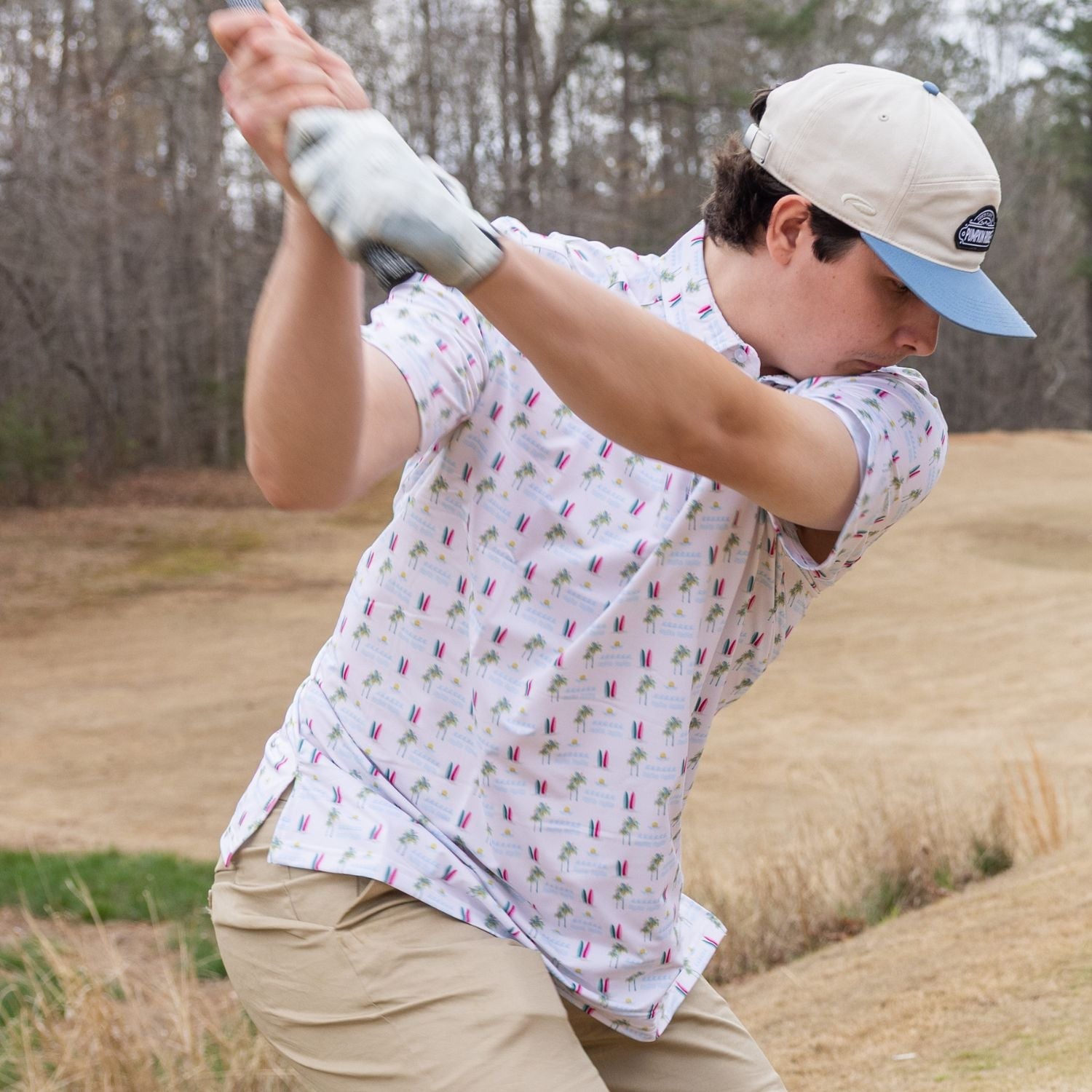Person playing golf in a patterned shirt and cap outdoors