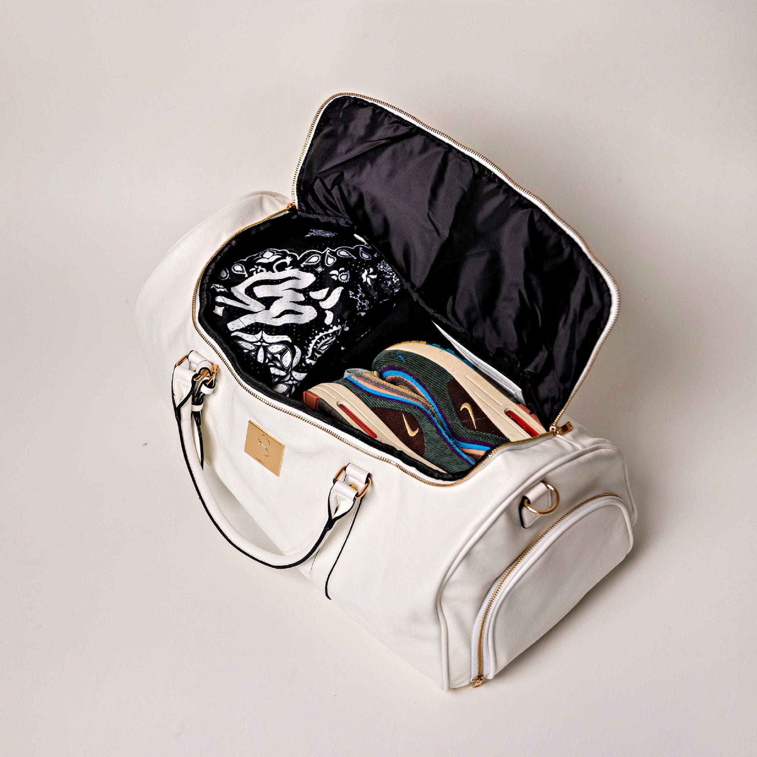 White handbag with open lid showing black interior and colorful shoes on a light gray background