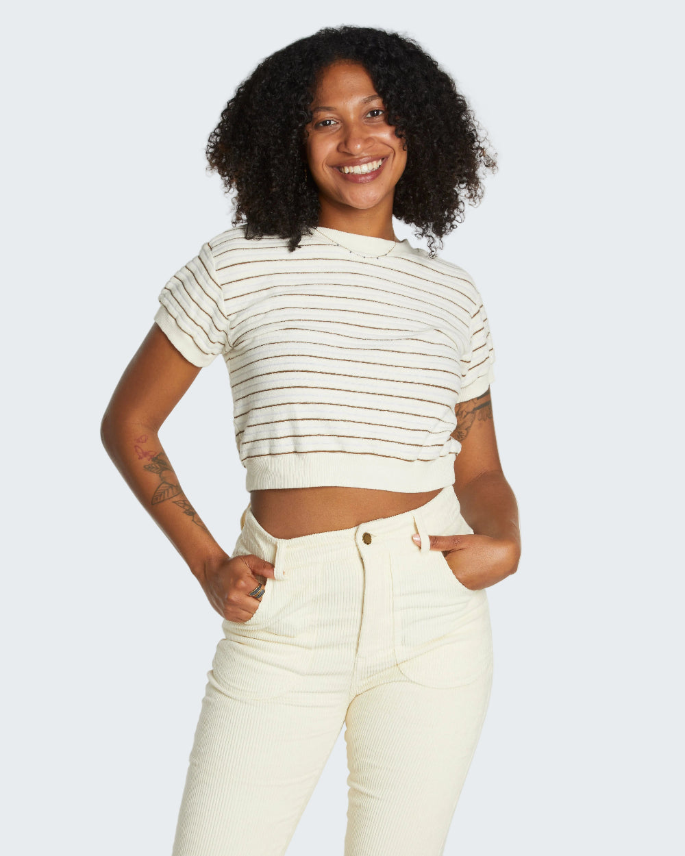 Woman wearing a striped crop top and high-waisted pants against a plain background