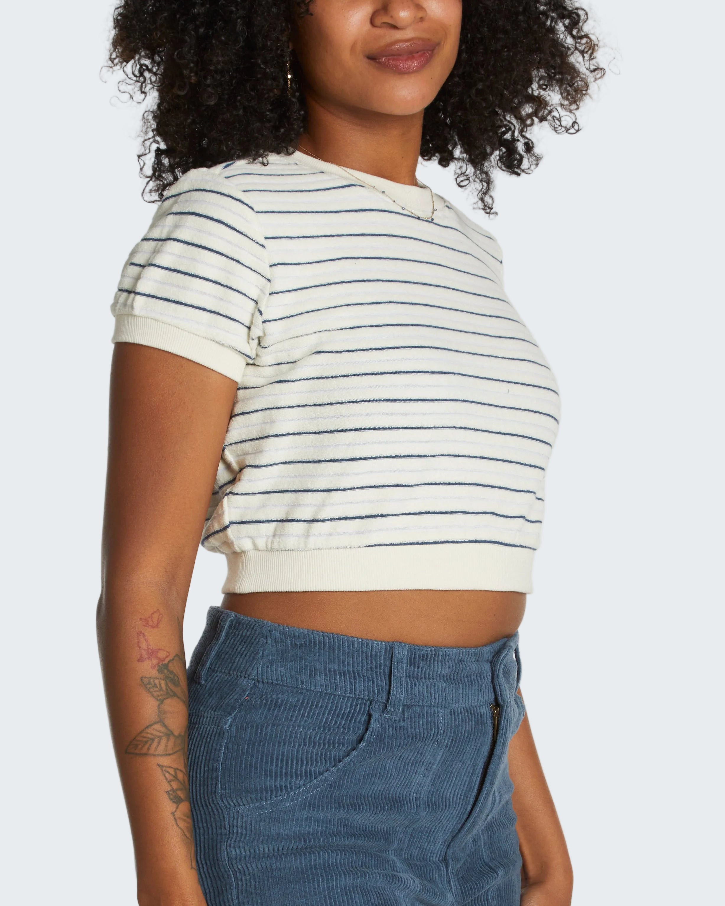 Person wearing a striped crop top and blue pants on a white background