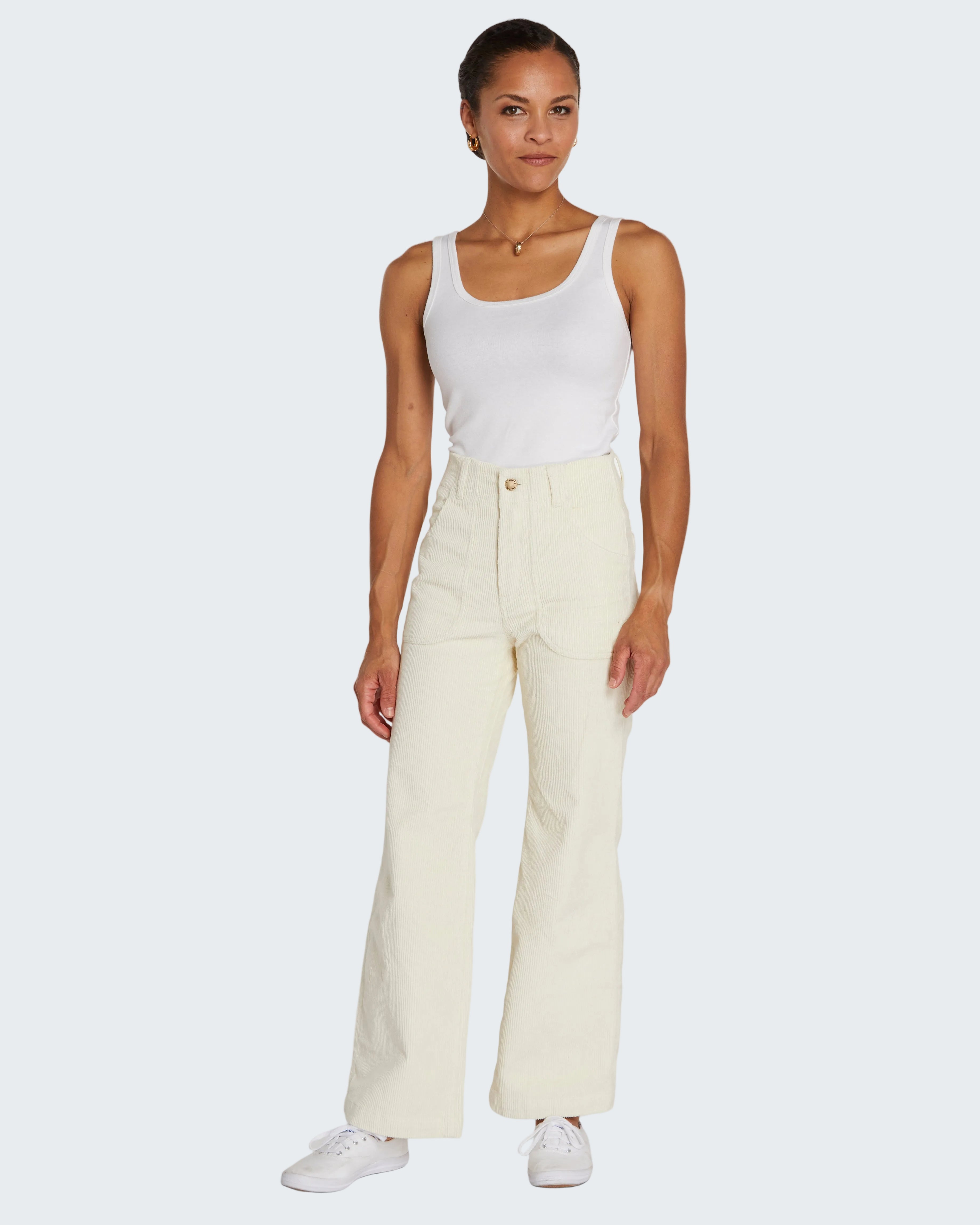 Woman wearing a white tank top and cream-colored pants on a white background