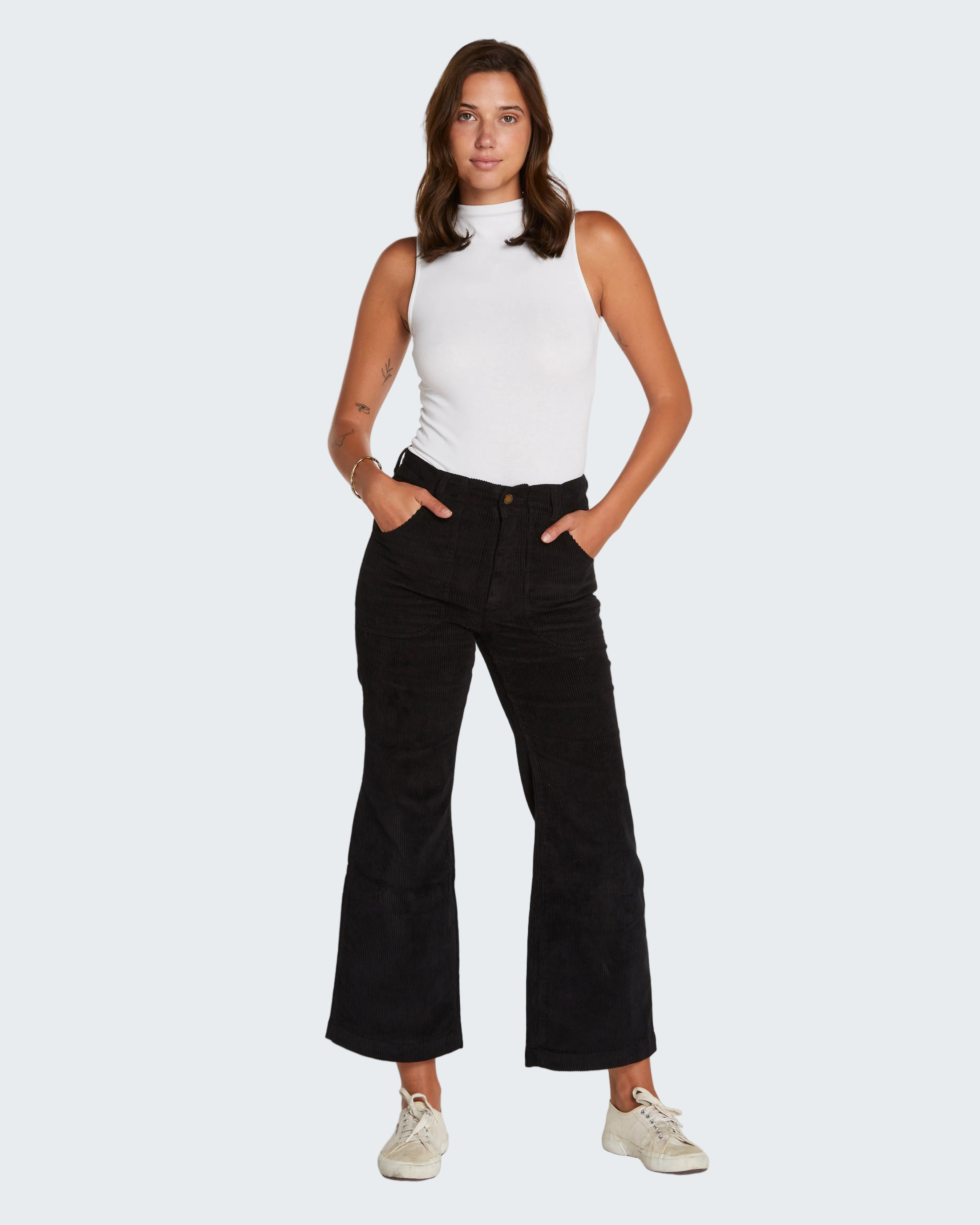 Woman wearing a white sleeveless top and black flared jeans on a white background