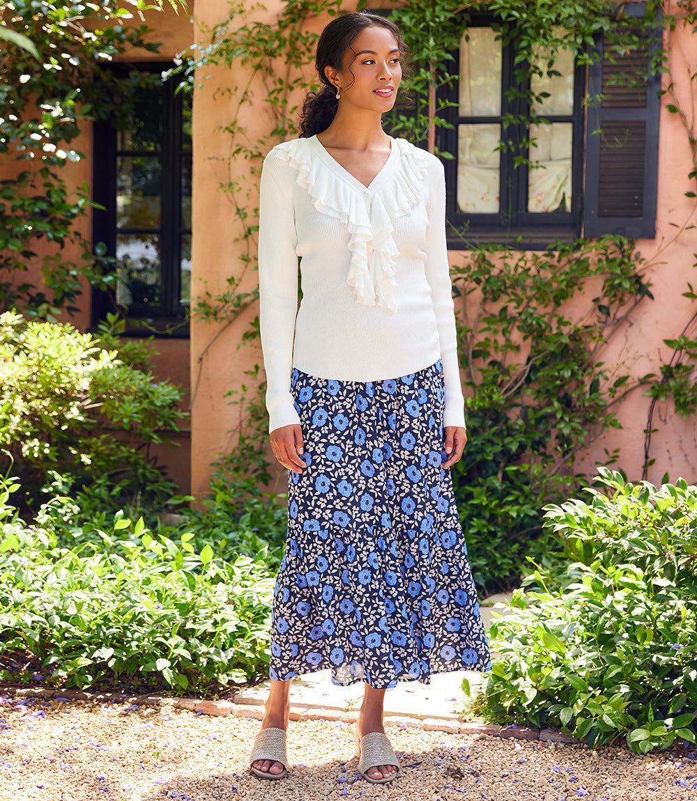 Woman wearing a white blouse and blue floral skirt standing in a garden.
