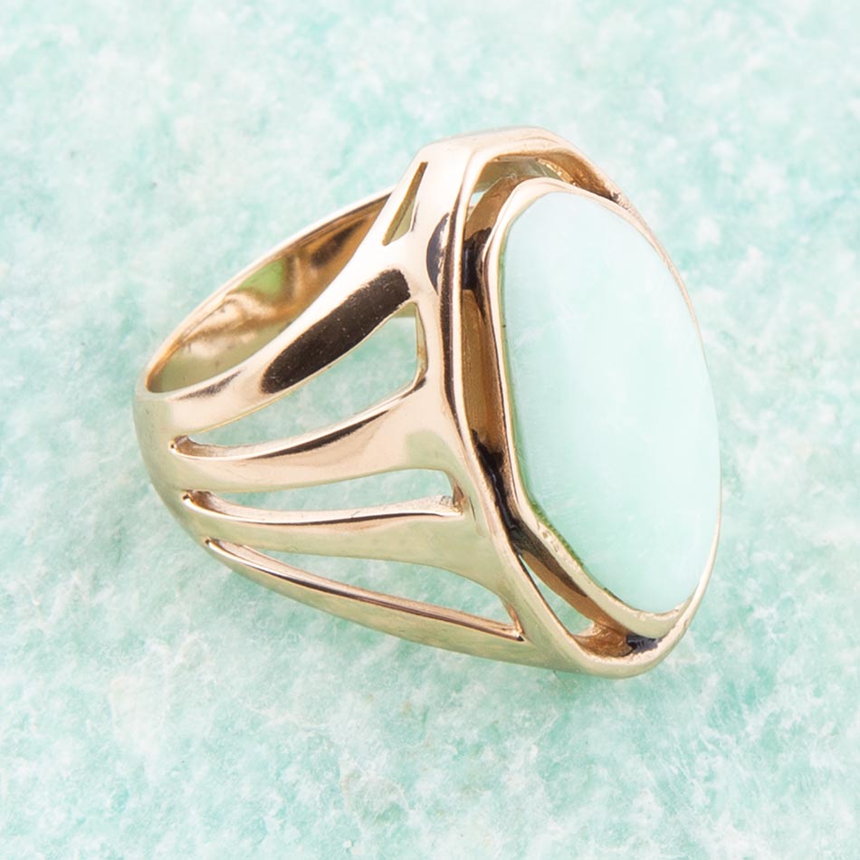 Gold ring with a light blue stone on a light green background