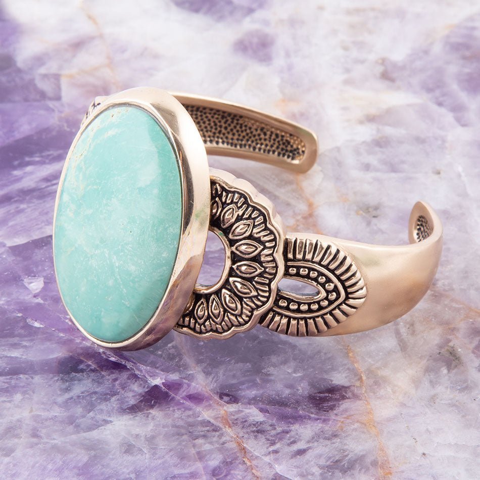 Gold bracelet with a turquoise stone on a purple marbled background
