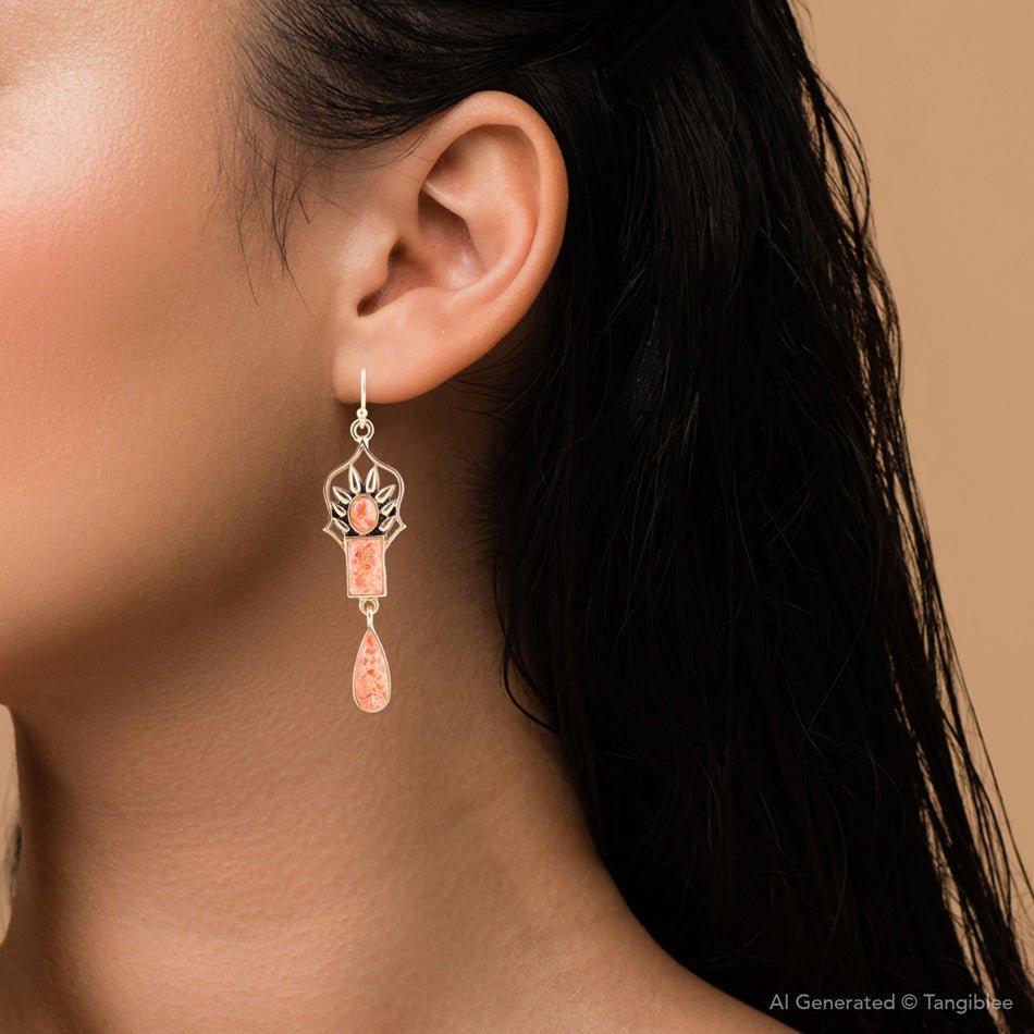Teardrop-shaped earring with a pink accent worn by a person on a beige background