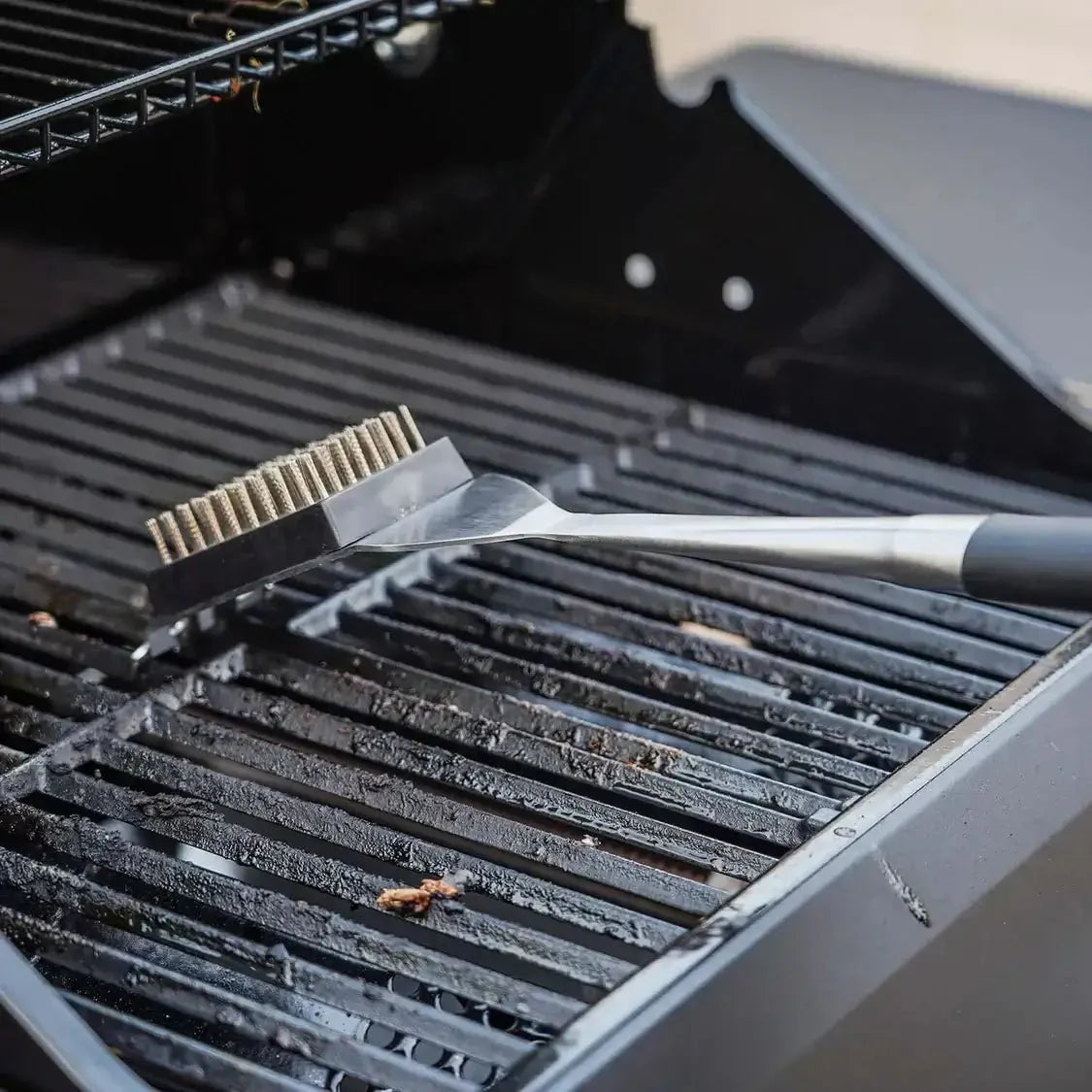Barbecue brush cleaning grill grates on an outdoor grill