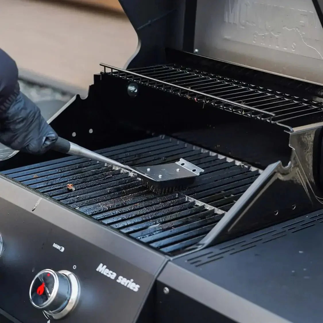 Person cleaning a Mesa Series grill with a brush