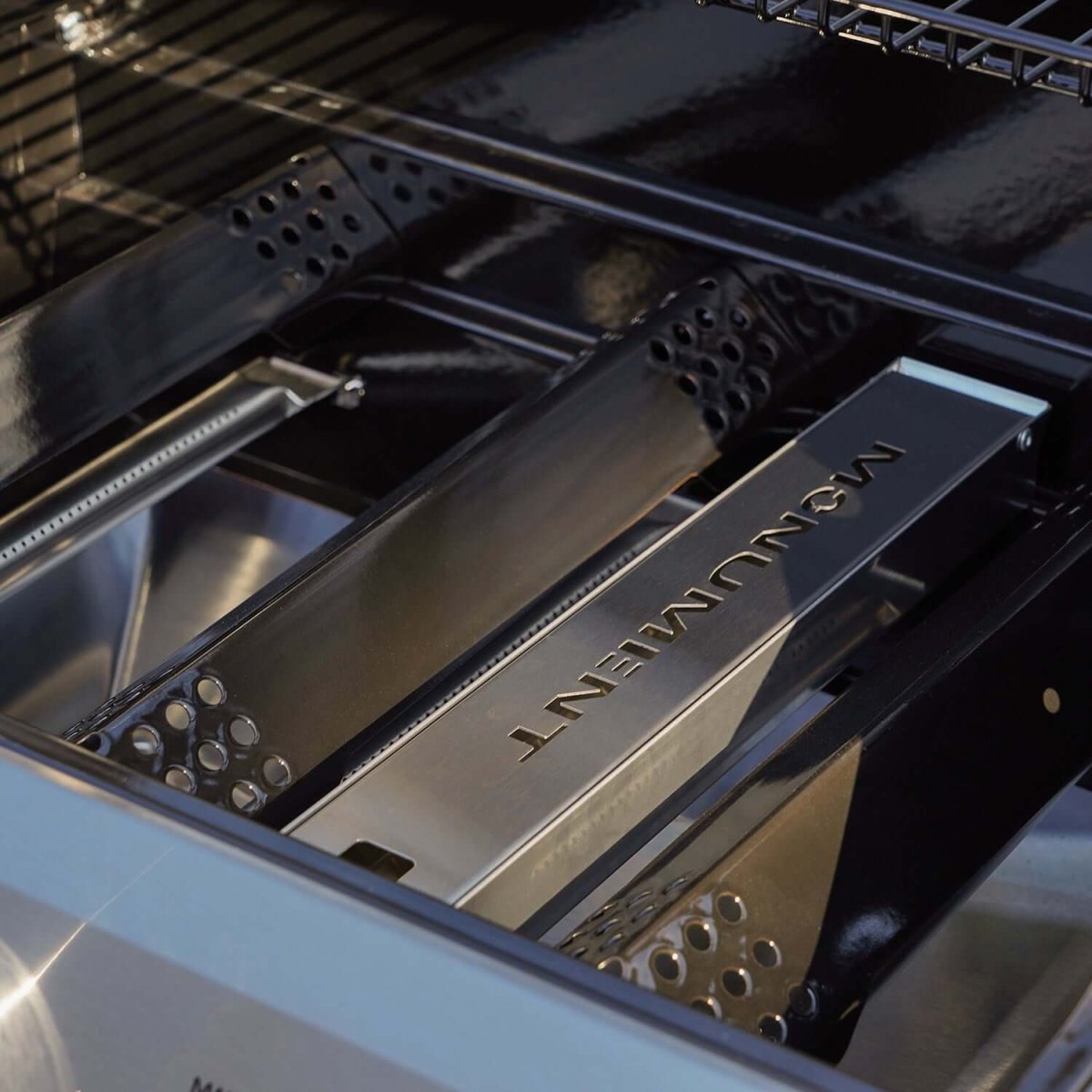 Metallic grill component with 'Moeniment' branding inside a barbecue.