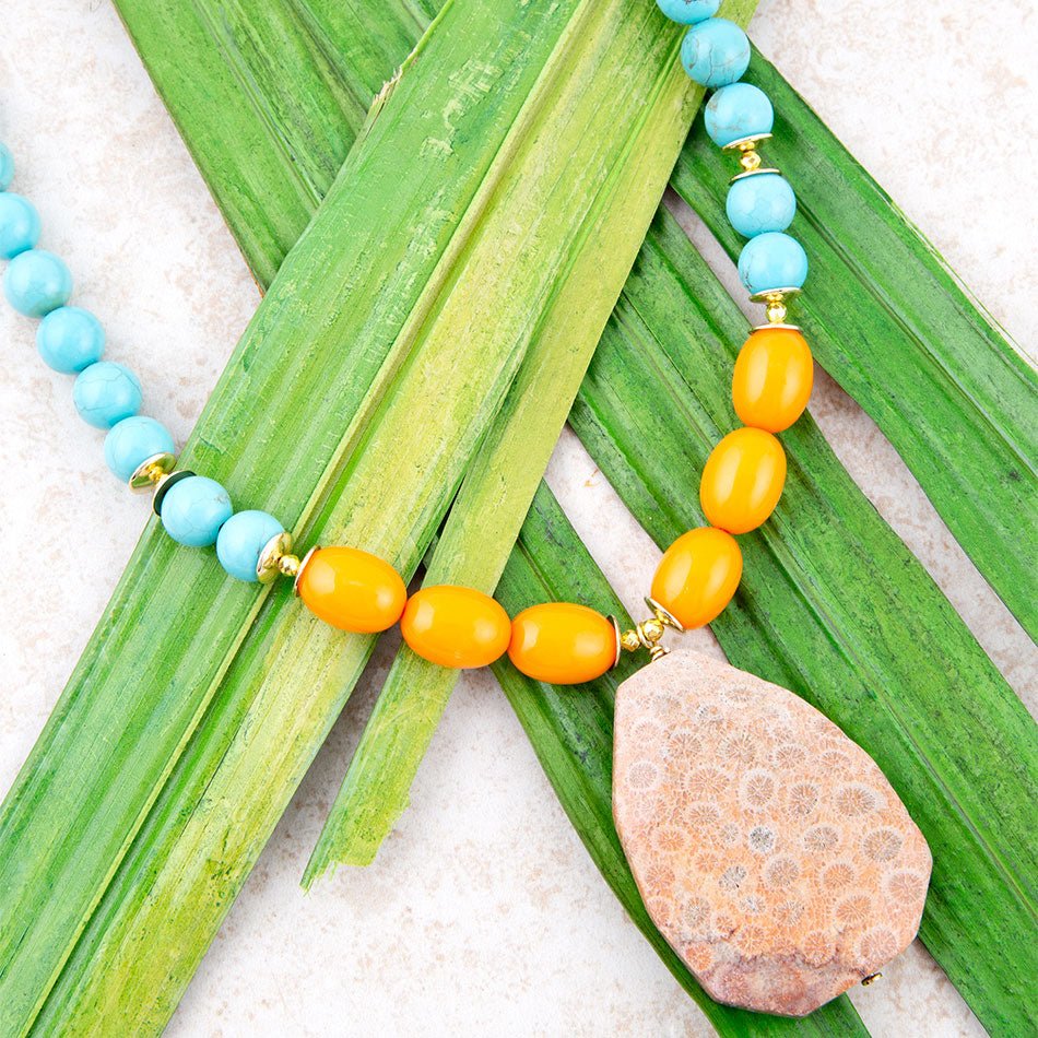 Necklace with blue and orange beads and a stone pendant on green leaves.