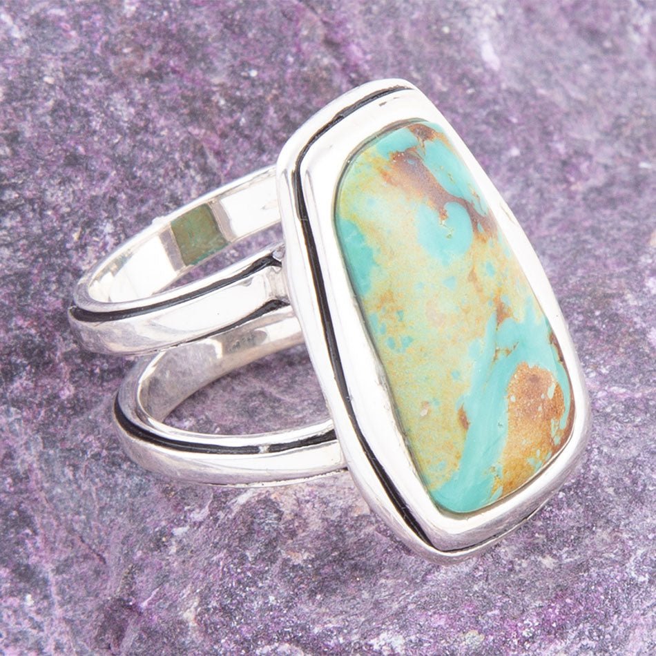 Turquoise stone ring with silver band on a purple textured background