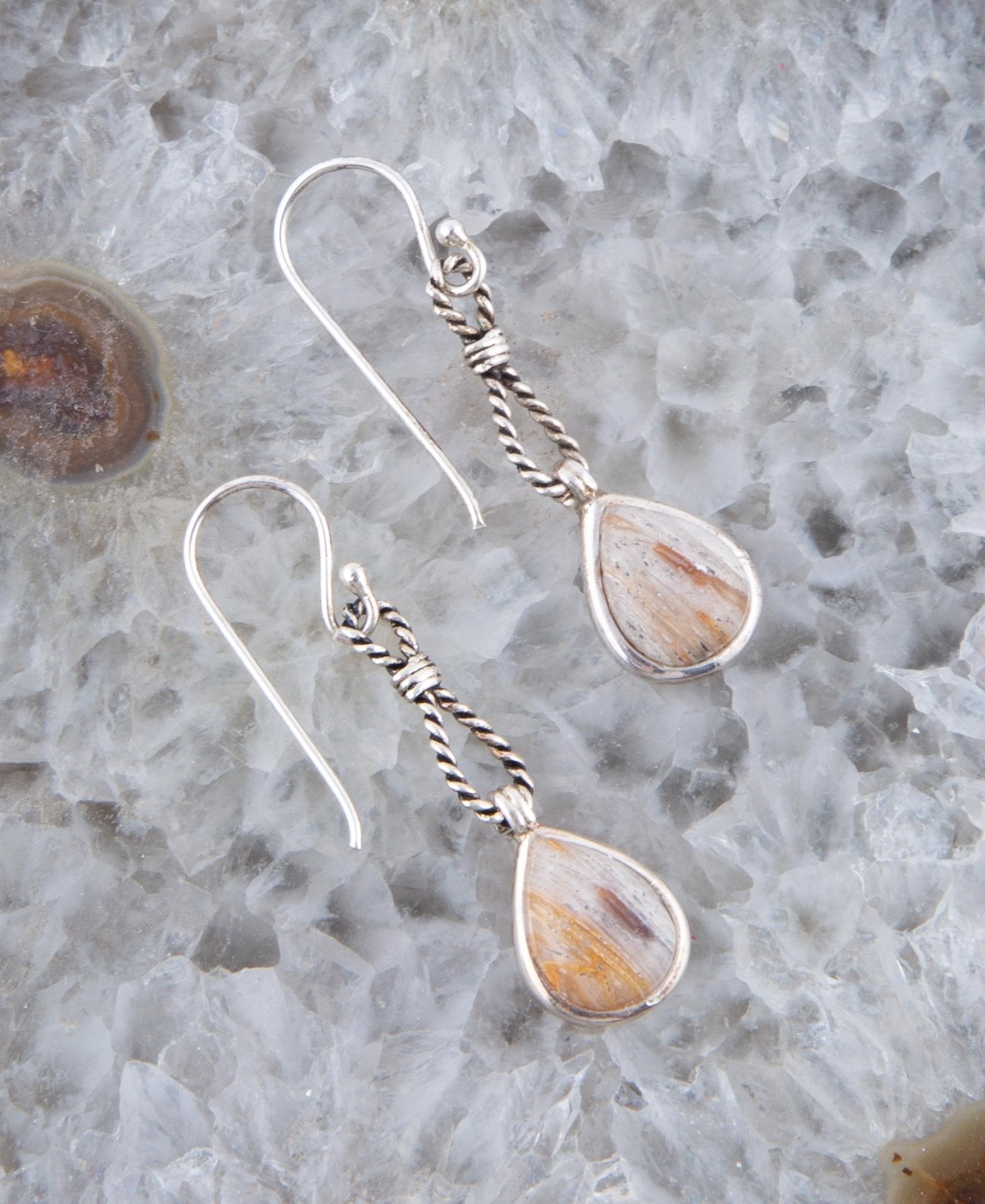 Teardrop-shaped earrings with silver hooks on a textured stone surface