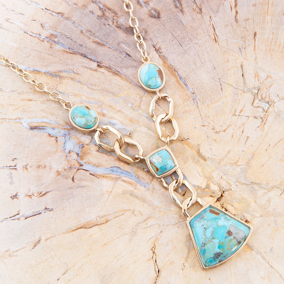 Gold necklace with turquoise stones on a beige stone surface