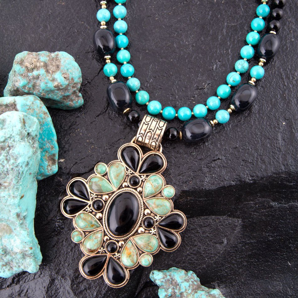 Necklace with turquoise and black beads and an ornate pendant on a dark surface.