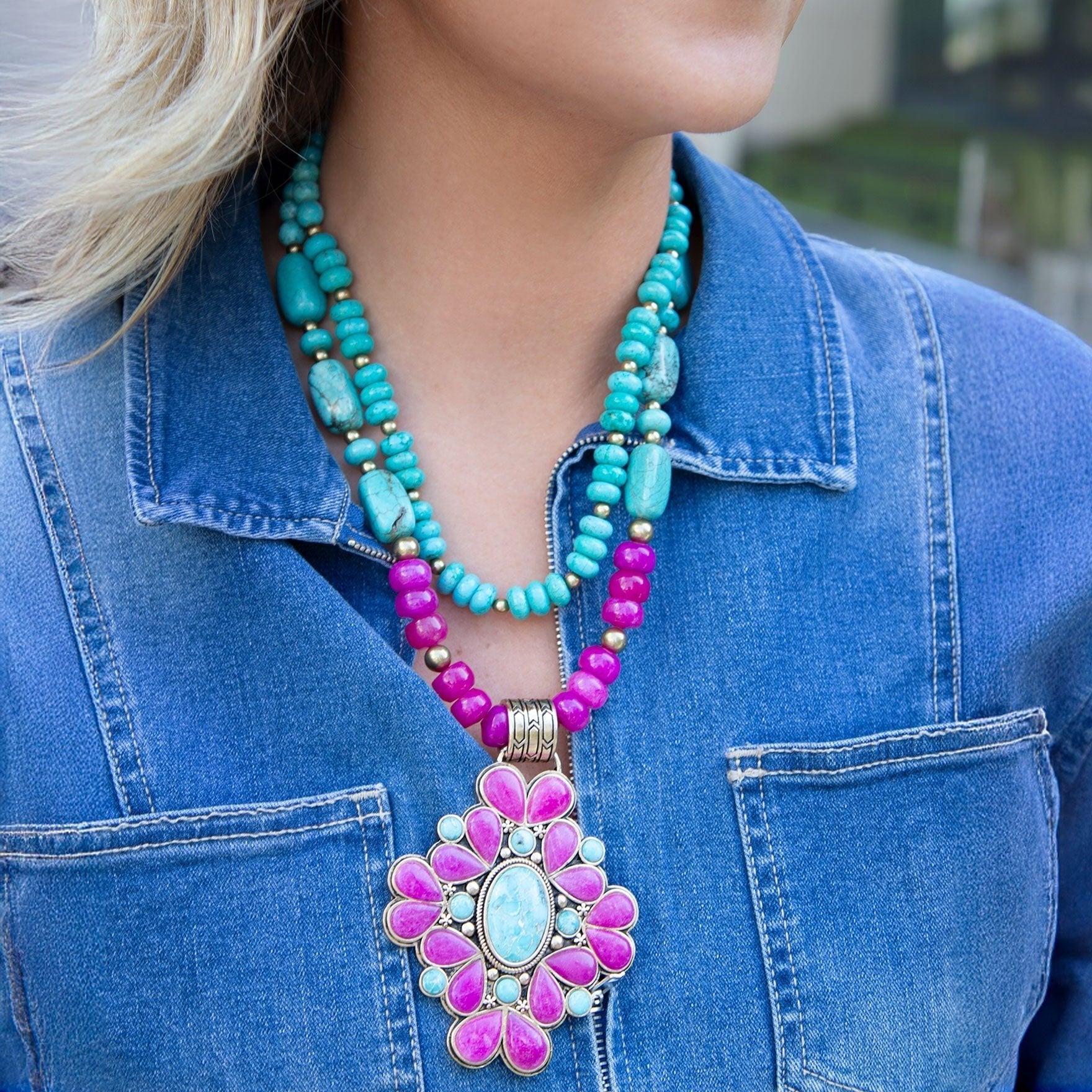 Turquoise and pink beaded necklace with a large floral pendant on a person wearing a blue denim jacket.