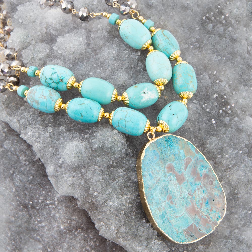 Turquoise beaded necklace with a large pendant on a textured gray surface