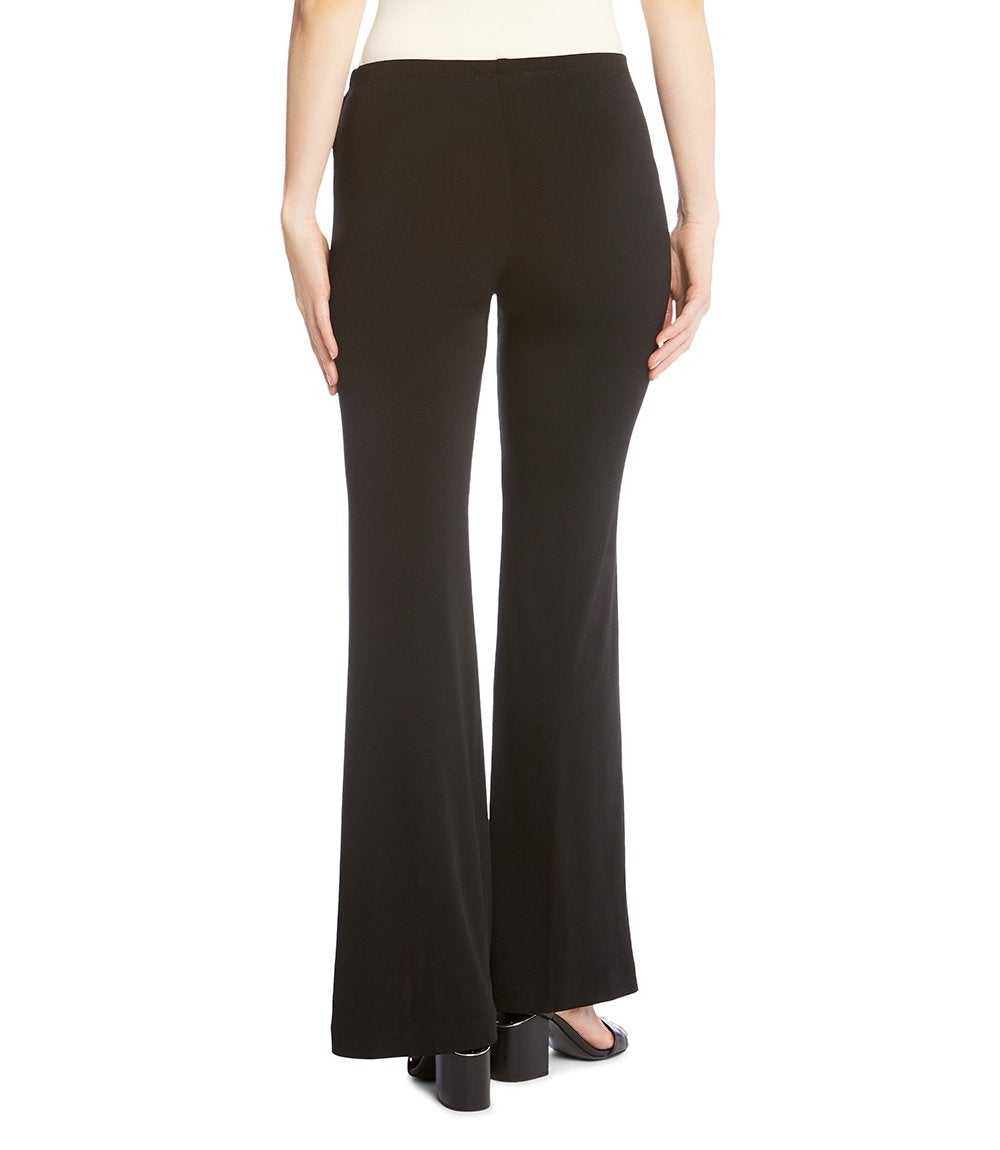 Black wide-leg flare pants shown on a model from the back, paired with a cream top and black block-heel sandals against a plain white background.