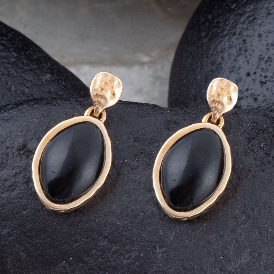 Pair of gold earrings with black stones on a dark surface