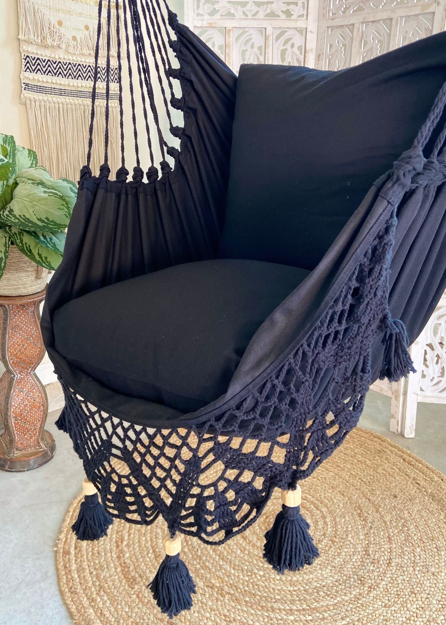 Black hammock chair with tassels on a textured floor