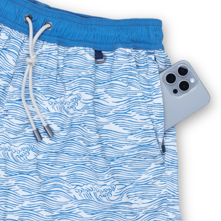 Blue swim shorts with wave pattern and white drawstring, next to a phone for size comparison.