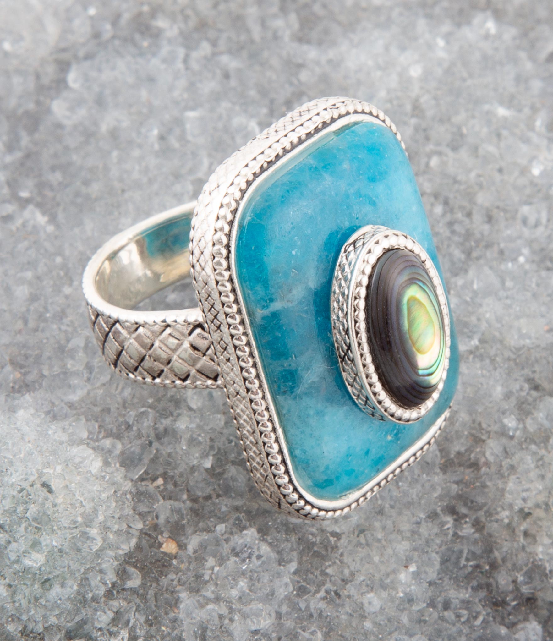 Silver ring with a blue stone and abalone shell on a gray surface