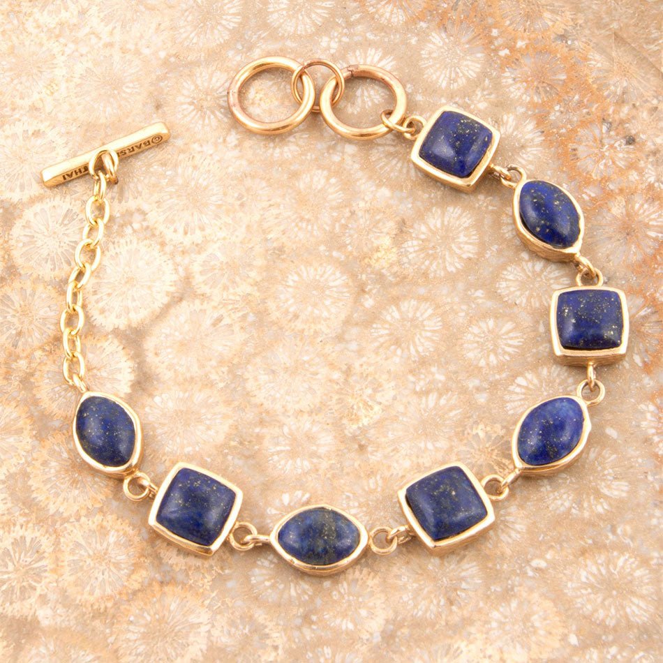 Gold bracelet with blue stones on a textured beige background