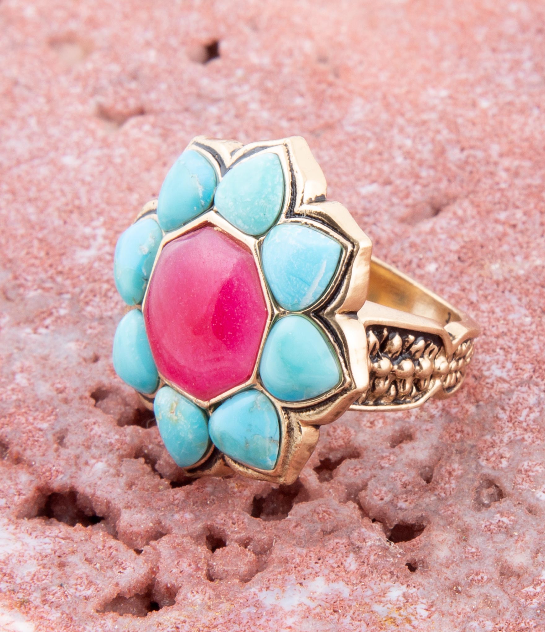 Ring with turquoise and pink stones on a textured pink surface