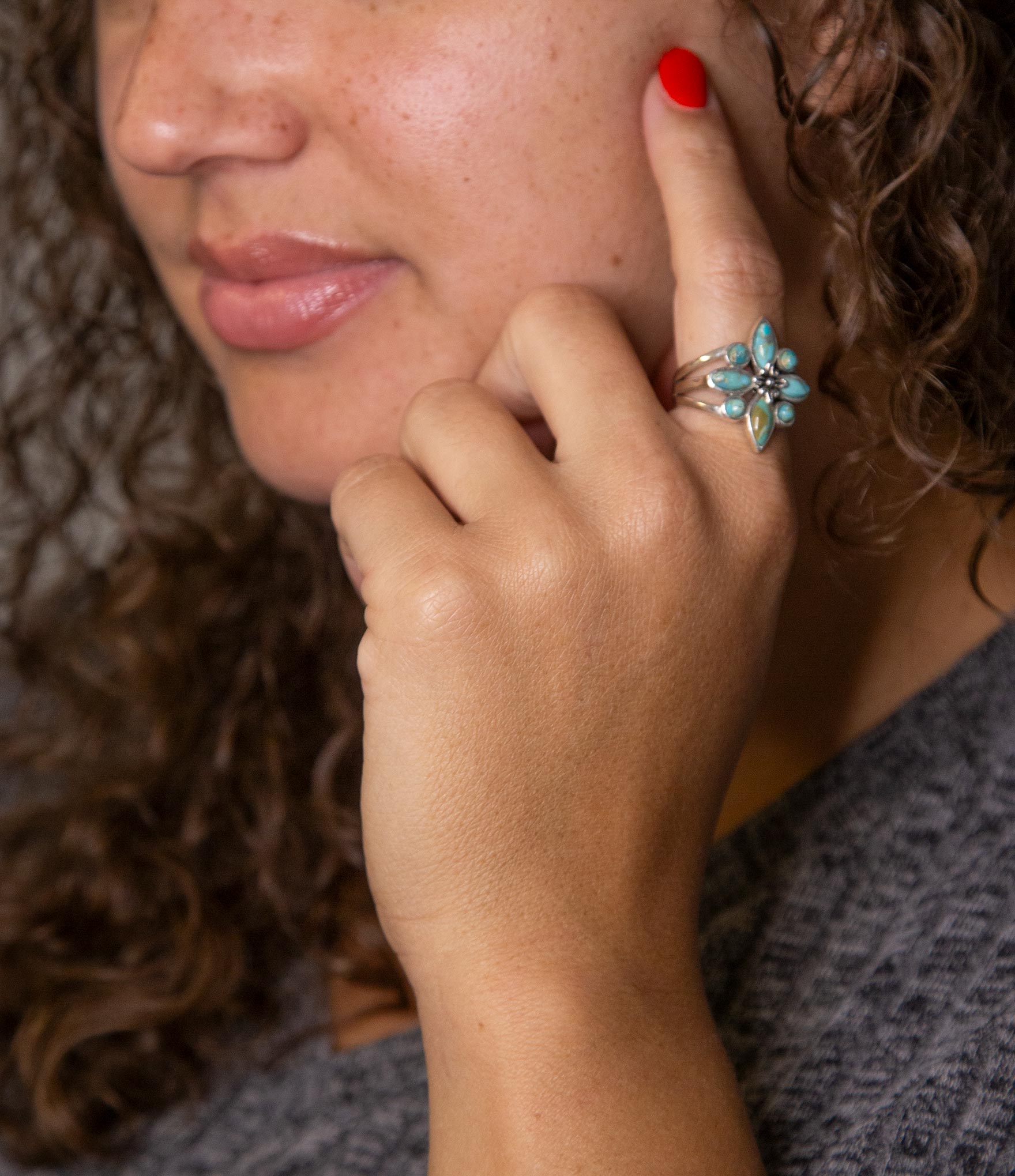 Close-up of a woman's hand with a ring, touching her face.
