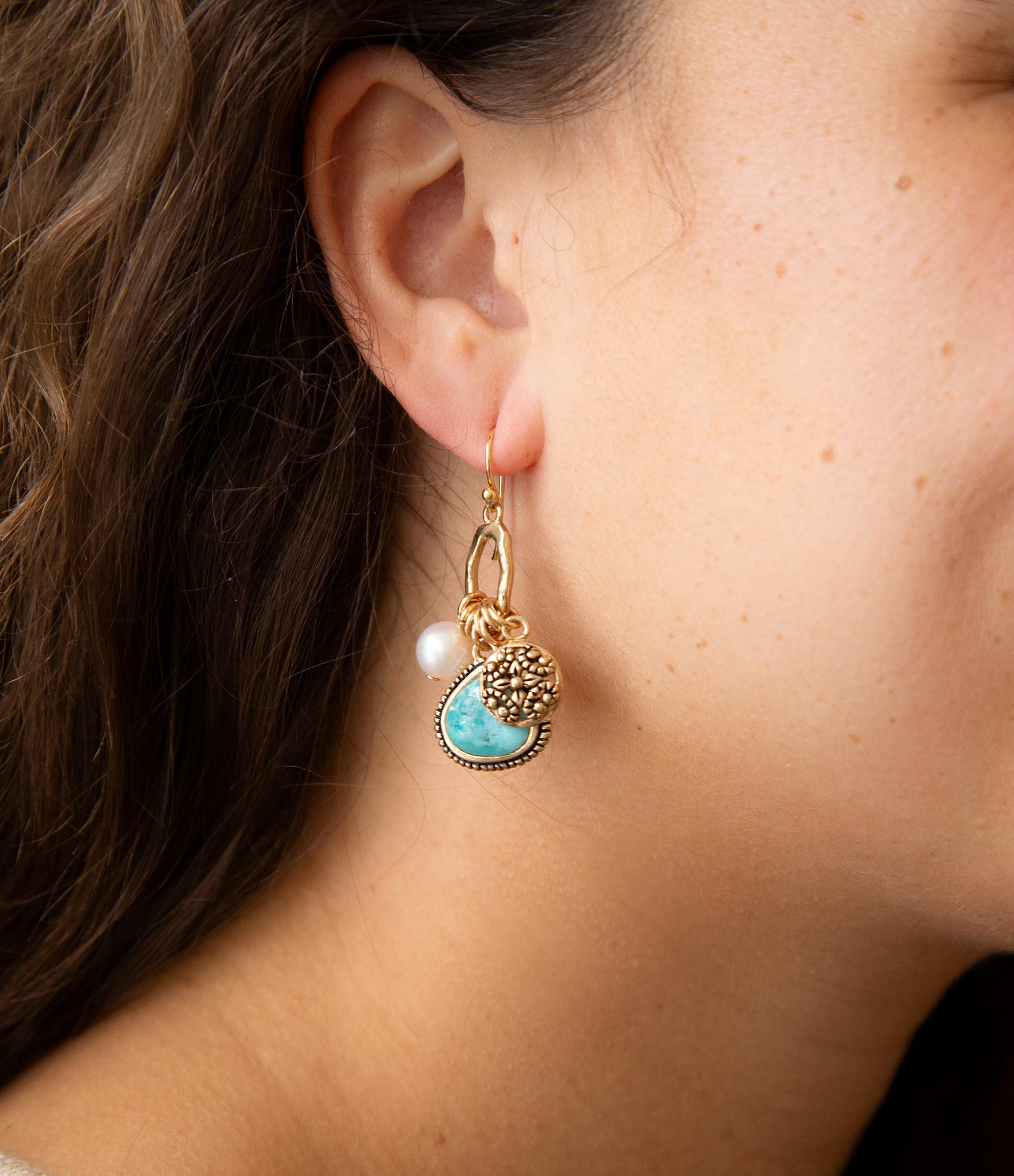 Close-up of a person wearing a gold earring with a turquoise stone and pearl.
