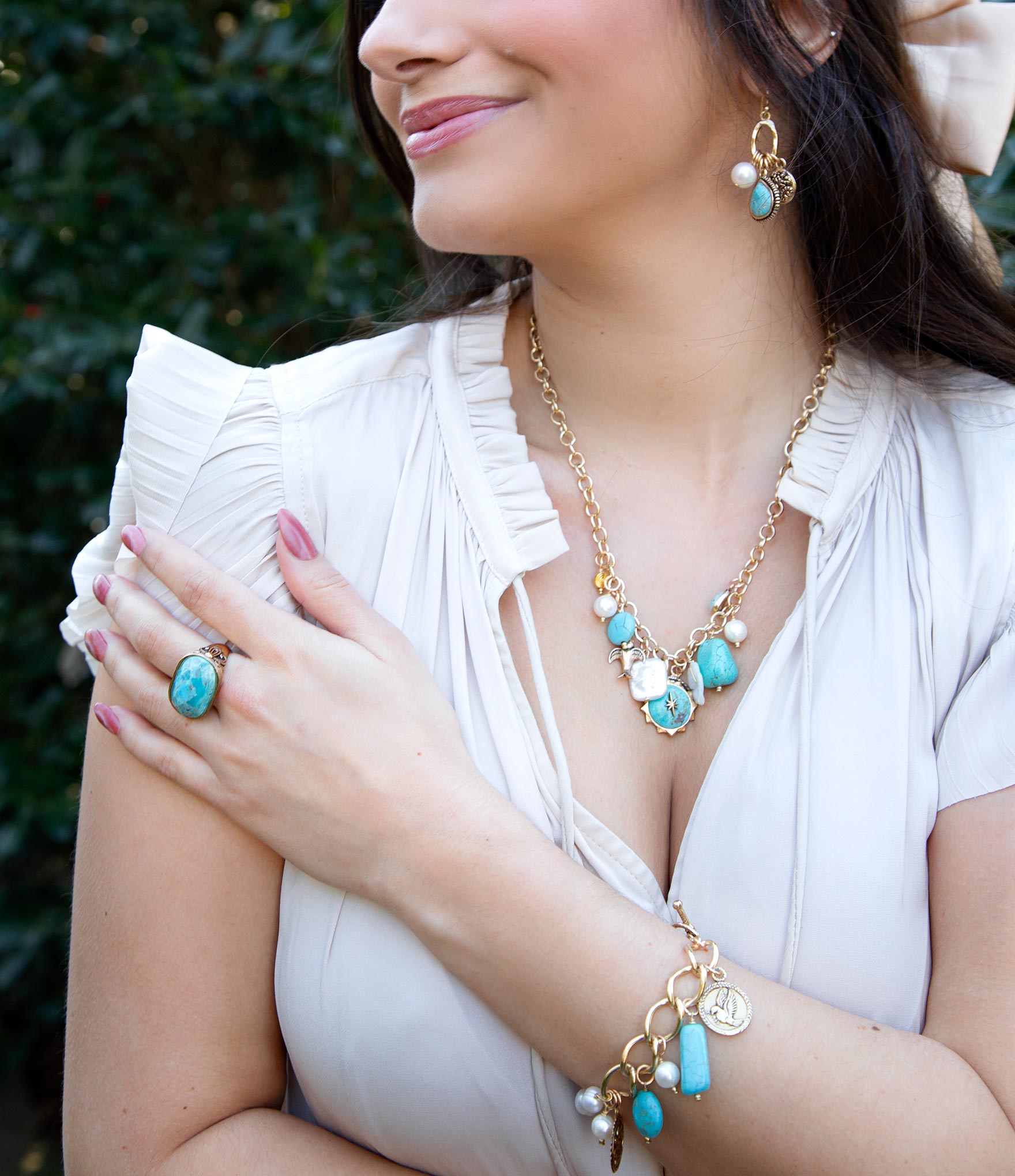 Woman wearing a gold and turquoise necklace, ring, and bracelet with a white top.