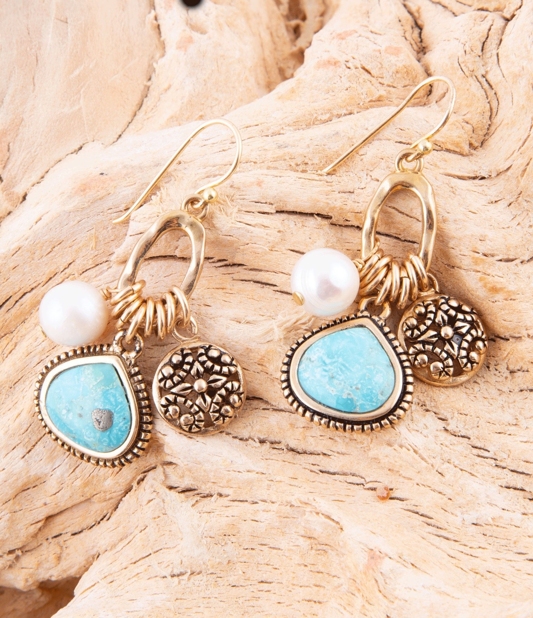 Gold and turquoise earrings with pearls on a wooden surface