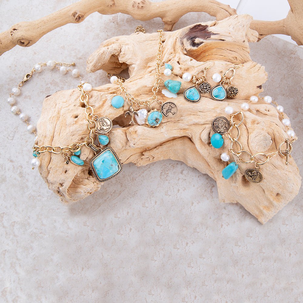 Gold bracelets with turquoise and pearl charms on a piece of driftwood.