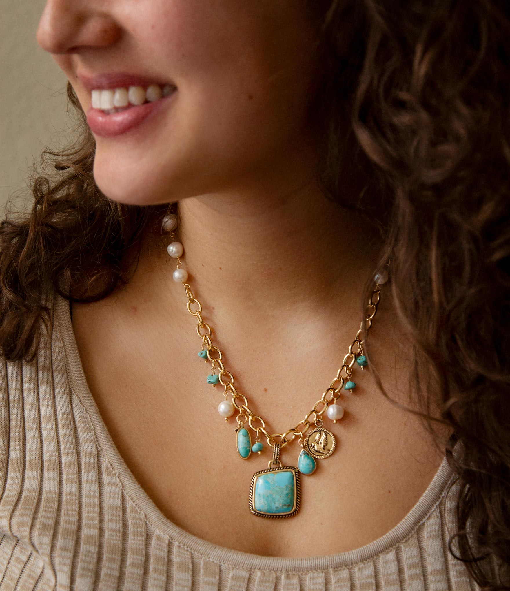 Close-up of a woman wearing a gold necklace with turquoise pendant and pearl accents.