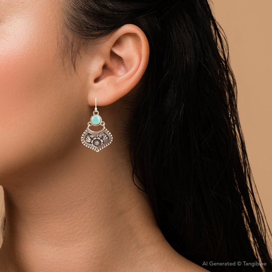 Close-up of an ear wearing a decorative earring with a turquoise gemstone on a neutral background.