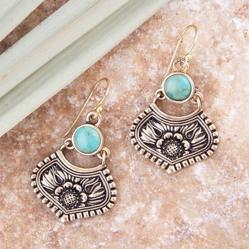 Pair of ornate earrings with turquoise stones on a textured surface